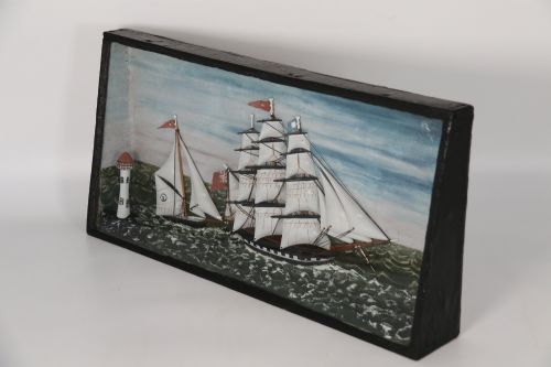fig 1. A nineteenth-century glass-fronted black wooden shadow box featuring a carved and painted diorama of two sailing ships and a lighthouse on a textured sea.