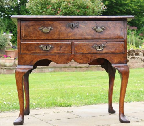 fig 1. A George II burr elm lowboy featuring three drawers, brass drop handles, a scalloped apron, and cabriole legs terminating in pad feet.