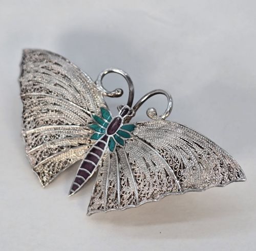fig 2. A silver filigree butterfly brooch featuring teal and purple enamelled body details.
