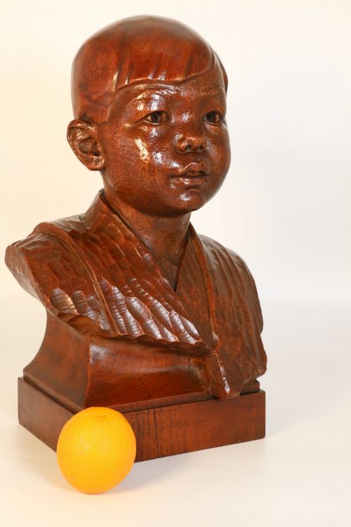 fig 1. A carved walnut sculpture bust of a young child set upon a matching rectangular wooden plinth.