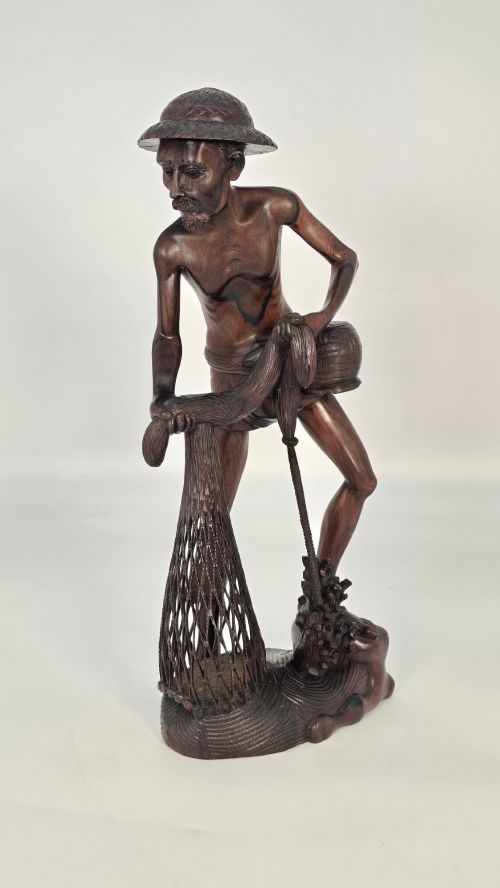 fig 2. A hand-carved dark hardwood sculpture depicting a standing fisherman holding a woven net and basket, set on an organic carved base.