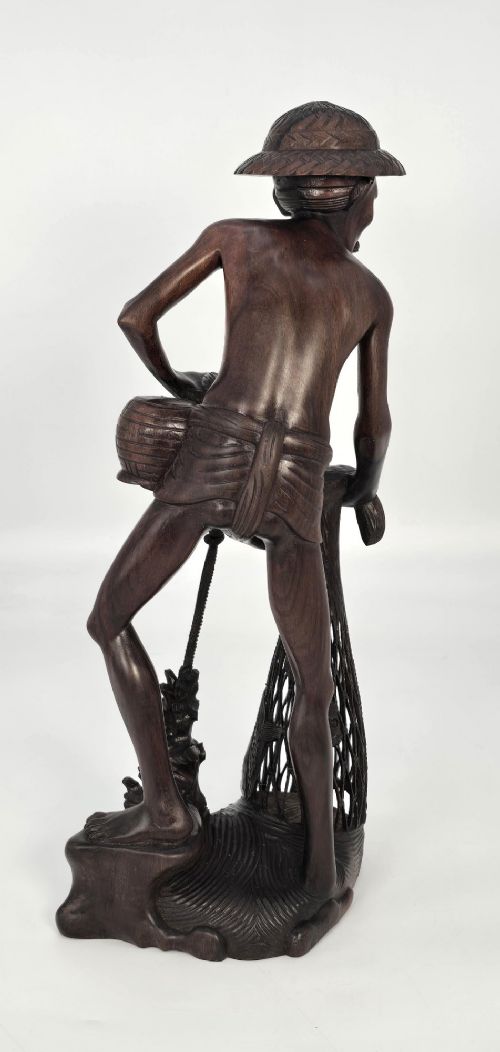 A hand-carved dark hardwood sculpture depicting a standing fisherman holding a woven net and basket, set on an organic carved base. View XIII