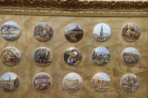fig 2. A large rectangular ornate gilt frame displaying thirty-five circular Victorian polychrome transfer-printed ceramic pot lids mounted in grid formation.