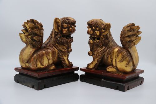 fig 2. A pair of hand-carved Chinese wooden guardian lions finished in gold gilding and red lacquer, seated on dark rectangular bases.