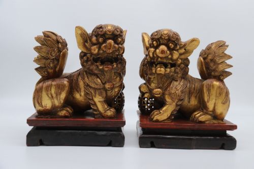 fig 3. A pair of hand-carved Chinese wooden guardian lions finished in gold gilding and red lacquer, seated on dark rectangular bases.