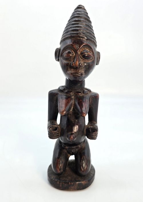 fig 1. A dark brown hand-carved wooden figure depicting a kneeling female with a tall ridged headpiece and carved facial markings.