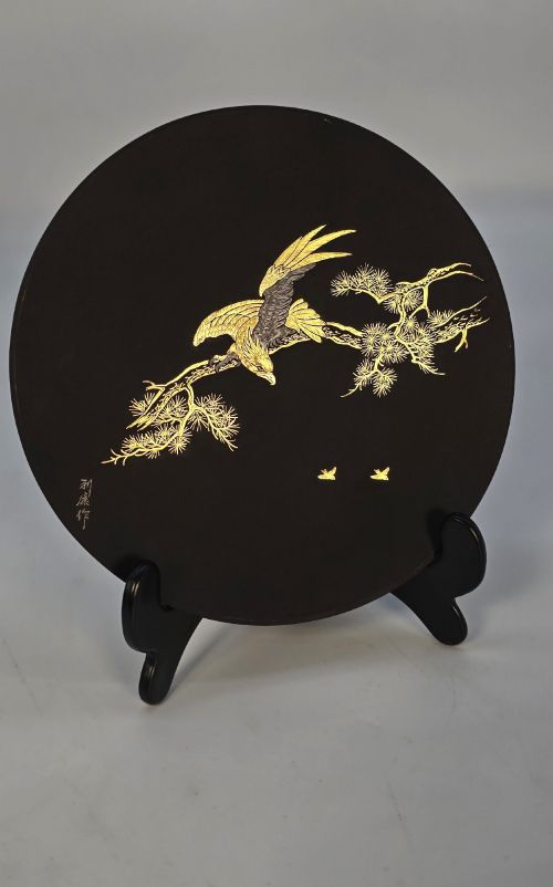 fig 1. A circular black patinated iron plaque featuring an inlaid gold and silver depiction of an eagle perched on a pine branch.
