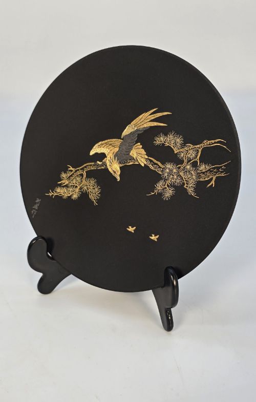 fig 2. A circular black patinated iron plaque featuring an inlaid gold and silver depiction of an eagle perched on a pine branch.