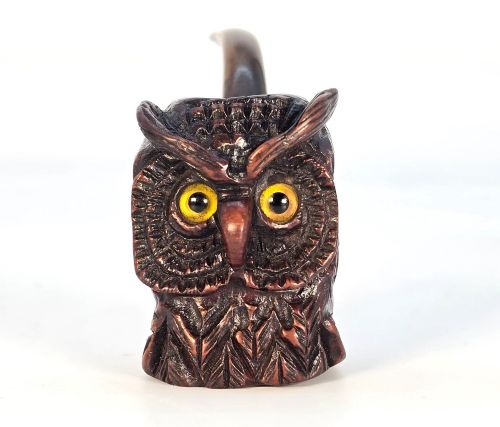 fig 2. A detailed hand-carved briar wood tobacco pipe crafted in the shape of an owls head featuring yellow glass eyes and a curved black stem.