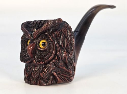 fig 3. A detailed hand-carved briar wood tobacco pipe crafted in the shape of an owls head featuring yellow glass eyes and a curved black stem.