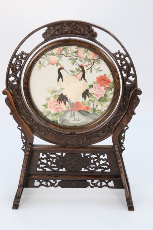 fig 2. A circular double-sided silk embroidery depicting cranes among pink flowers, set within a rotating carved dark hardwood frame and stand.