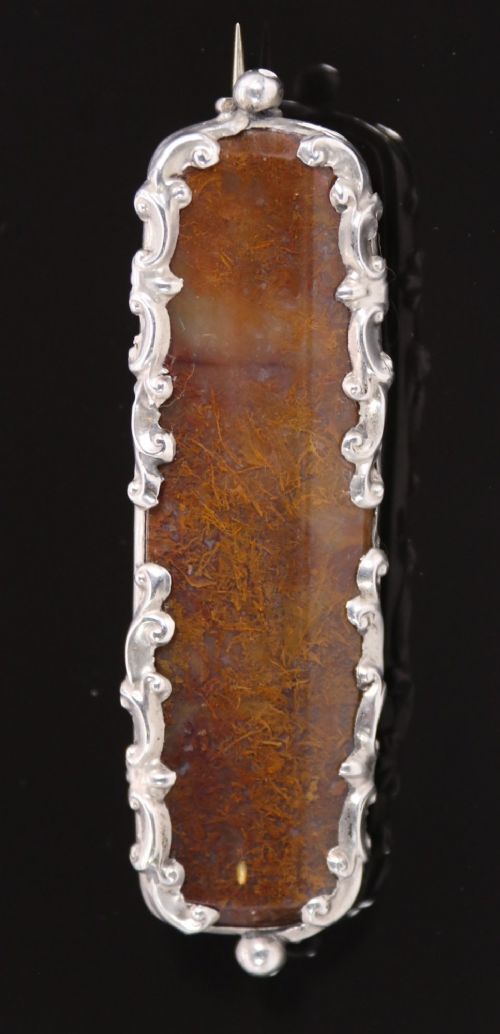 An elongated Georgian silver bar brooch featuring a rectangular polished moss agate panel with a scrollwork silver border. View VI