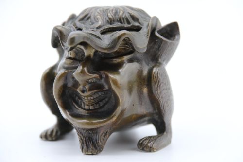fig 2. A dark cast bronze novelty inkwell sculpted in the form of a grotesque grinning face with textured hair and small footed base.