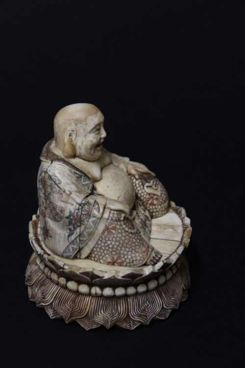 fig 2. A Japanese carved bone okimono depicting a seated Buddha figure on an engraved lotus base with intricate ink detailing.