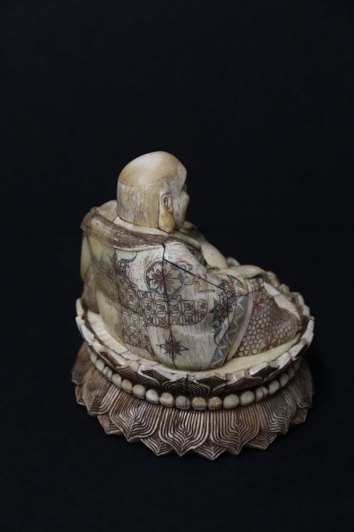 fig 3. A Japanese carved bone okimono depicting a seated Buddha figure on an engraved lotus base with intricate ink detailing.