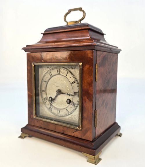fig 2. A miniature George II style wooden bracket clock featuring a caddy top with brass handle, engraved silvered dial with Roman numerals, and brass feet.