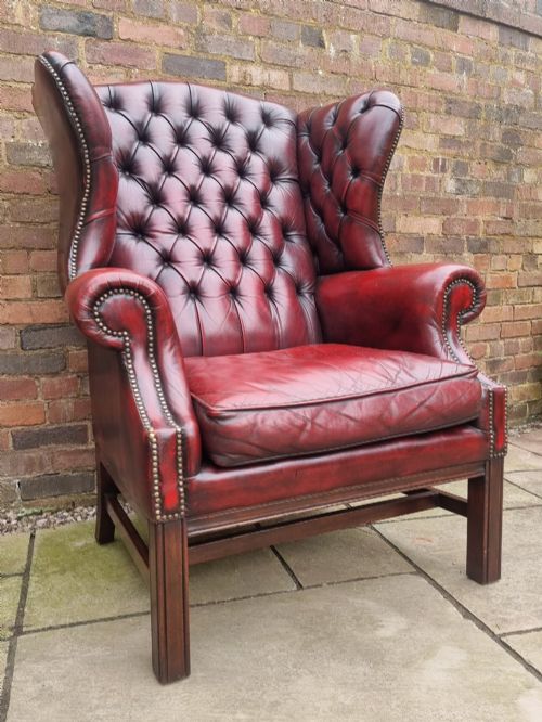 fig 2. A George III style wingback armchair upholstered in deep buttoned burgundy red leather with brass stud detailing and square mahogany legs.