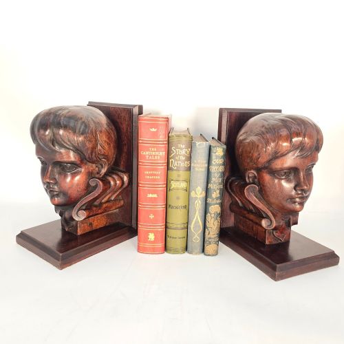 fig 1. A pair of carved mahogany bookends featuring profile busts of children mounted on L-shaped wooden bases.