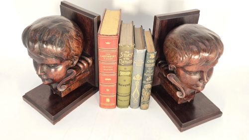 fig 2. A pair of carved mahogany bookends featuring profile busts of children mounted on L-shaped wooden bases.