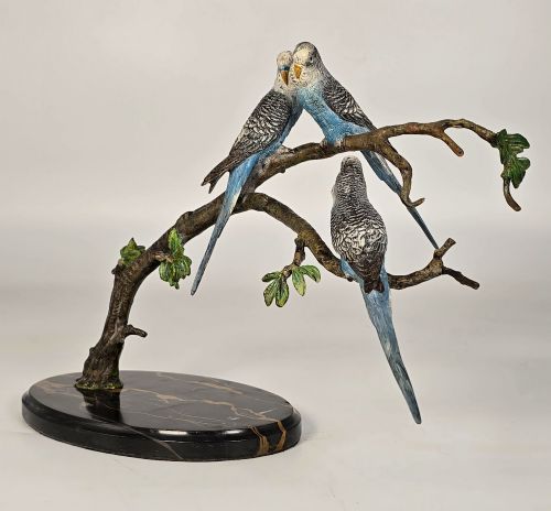 fig 1. A cold-painted bronze sculpture featuring three blue and grey budgerigars perched on a leafy bronze branch, mounted on an oval dark marble base.
