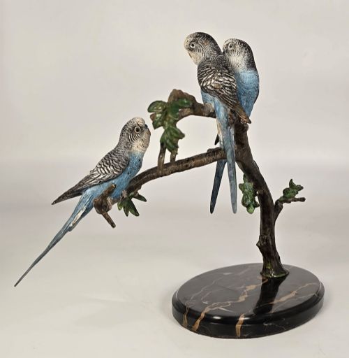 fig 3. A cold-painted bronze sculpture featuring three blue and grey budgerigars perched on a leafy bronze branch, mounted on an oval dark marble base.