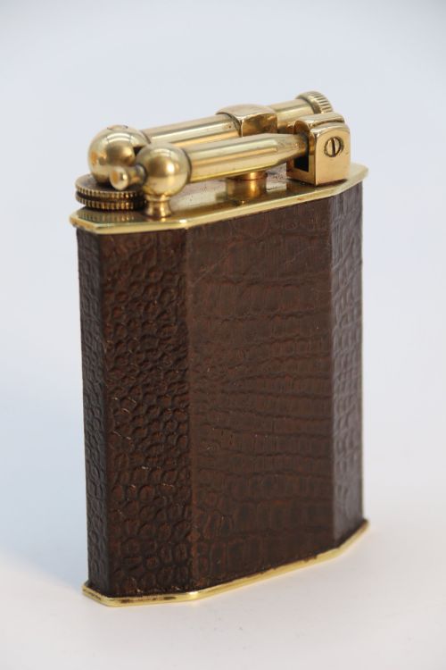 fig 1. An Art Deco French table lighter featuring a textured brown leather-wrapped faceted body and a polished brass lift-arm ignition mechanism.