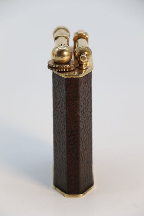 fig 2. An Art Deco French table lighter featuring a textured brown leather-wrapped faceted body and a polished brass lift-arm ignition mechanism.