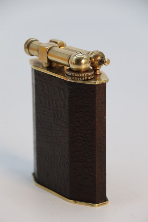 fig 3. An Art Deco French table lighter featuring a textured brown leather-wrapped faceted body and a polished brass lift-arm ignition mechanism.