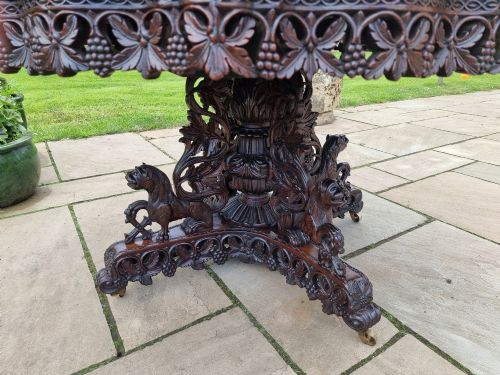 fig 4. A mid-19th century Anglo-Indian padauk centre table featuring a scalloped edge top, deeply carved pierced floral apron, and a central pedestal supported by carved lion figures on castors.