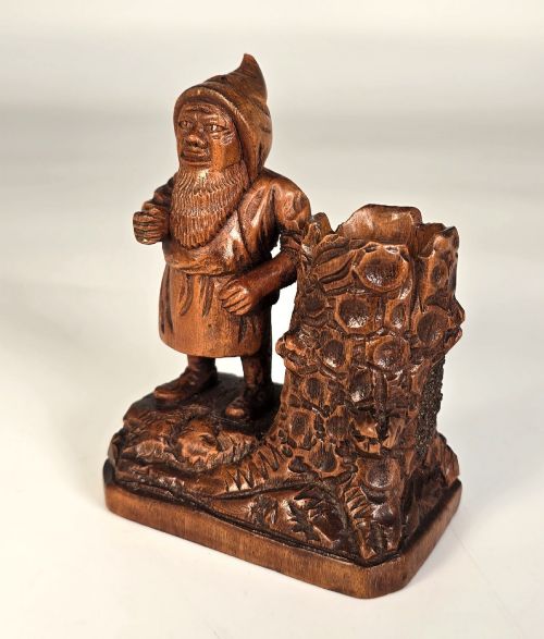 fig 1. A carved brown limewood match holder depicting a hooded bearded gnome standing beside a textured tree stump container.