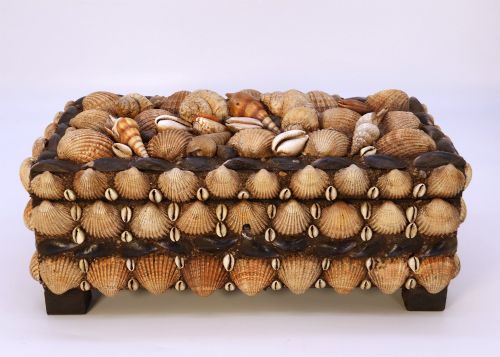fig 1. A rectangular wooden box encrusted entirely with an assortment of natural seashells, supported by four short block feet.