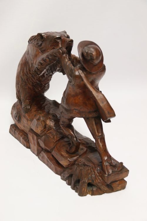 fig 1. A detailed 19th-century carved walnut sculpture depicting a man in traditional attire struggling with a standing bear upon a carved log base.
