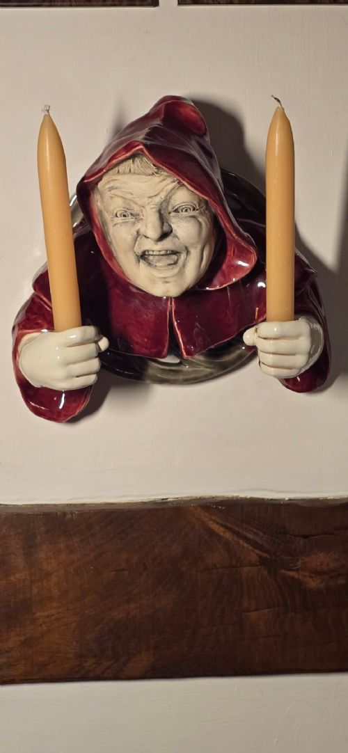 fig 1. A glazed ceramic wall-mounted candelabra depicting a hooded monk in a red cowl holding two candle sockets.