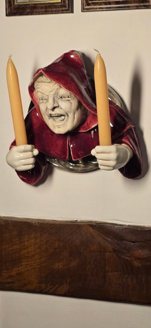 A glazed ceramic wall-mounted candelabra depicting a hooded monk in a red cowl holding two candle sockets. View III
