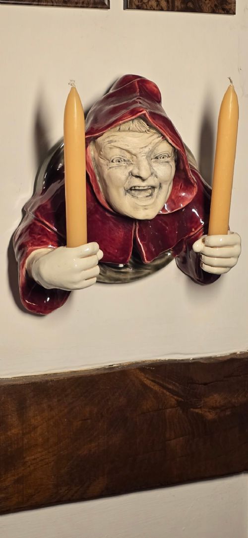 A glazed ceramic wall-mounted candelabra depicting a hooded monk in a red cowl holding two candle sockets. View IV