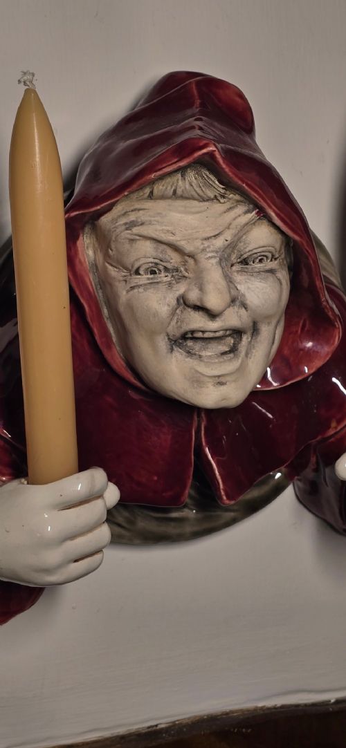 A glazed ceramic wall-mounted candelabra depicting a hooded monk in a red cowl holding two candle sockets. View V