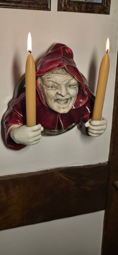 A glazed ceramic wall-mounted candelabra depicting a hooded monk in a red cowl holding two candle sockets. View VI