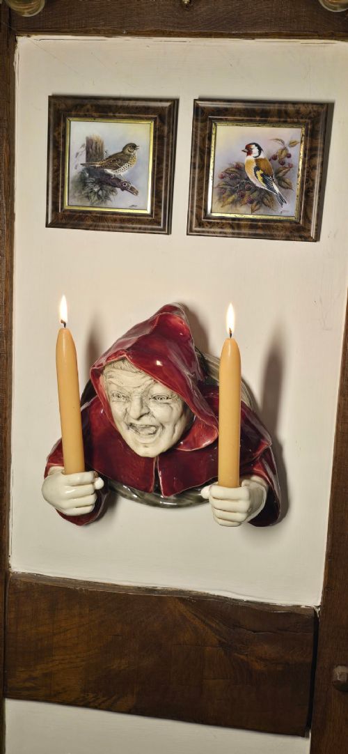 A glazed ceramic wall-mounted candelabra depicting a hooded monk in a red cowl holding two candle sockets. View VII