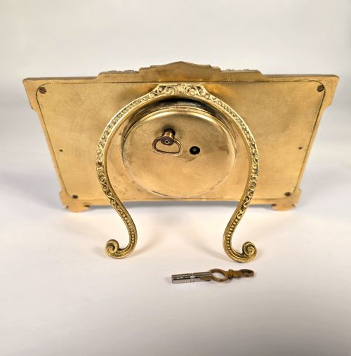fig 3. A rectangular gilt brass Art Deco strut clock featuring an illustrated courtly scene on the central dial surrounded by numeric markers.