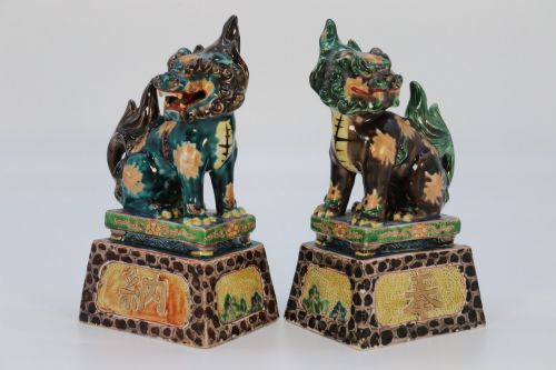 fig 1. A pair of glazed Chinese ceramic Buddhist lion figures decorated in green, brown, and yellow glazes resting on patterned pedestal bases.