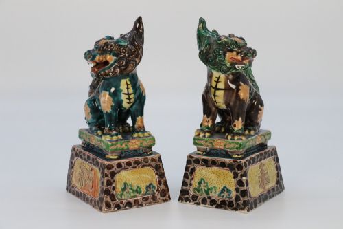 fig 2. A pair of glazed Chinese ceramic Buddhist lion figures decorated in green, brown, and yellow glazes resting on patterned pedestal bases.