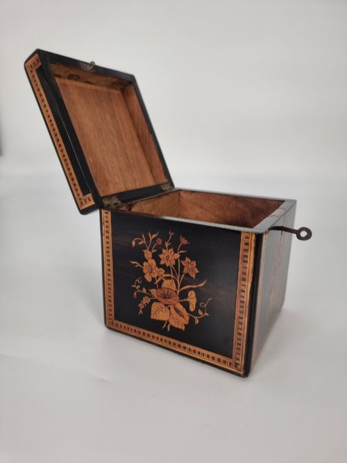 fig 2. A square ebonised wooden box featuring detailed Sorrento marquetry inlay depicting figures on the top lid, floral motifs on the sides, and geometric borders.