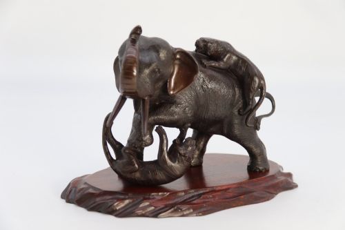 fig 1. A dark patinated bronze sculpture of an elephant defending itself against two tigers, mounted on a carved wooden base.