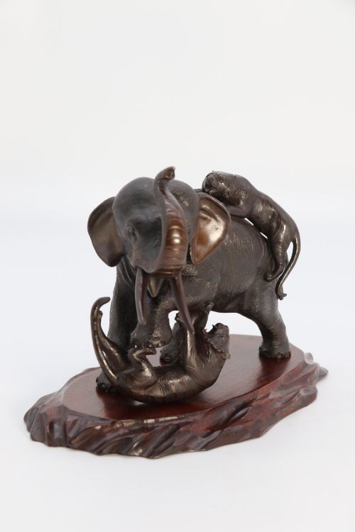fig 2. A dark patinated bronze sculpture of an elephant defending itself against two tigers, mounted on a carved wooden base.