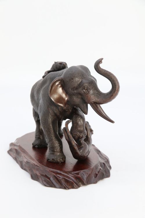 fig 3. A dark patinated bronze sculpture of an elephant defending itself against two tigers, mounted on a carved wooden base.