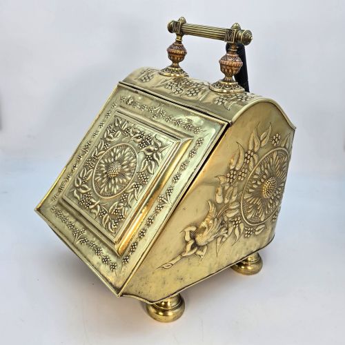 fig 2. Victorian sloped brass coal box featuring repousse sunflower motifs, turned brass feet, and a top carrying handle with an integrated rear shovel.