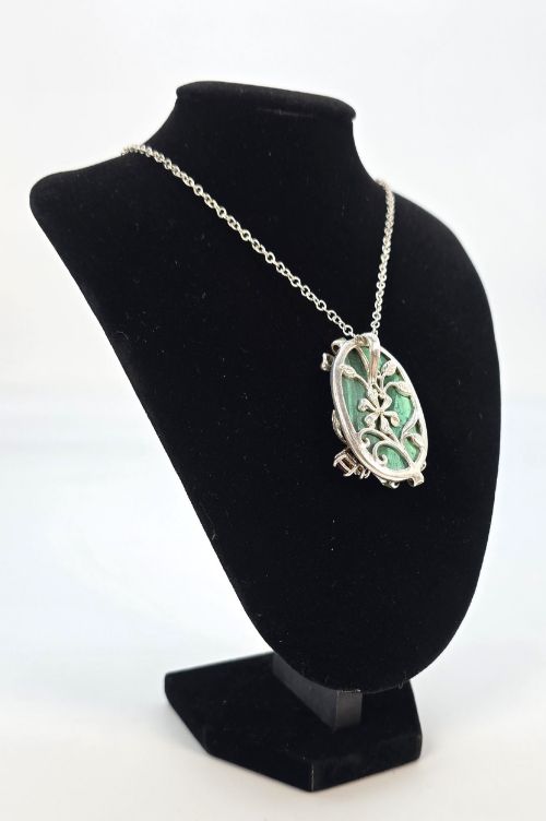 fig 3. An oval green malachite pendant framed in silver metalwork with enamelled floral motifs, attached to a silver chain.