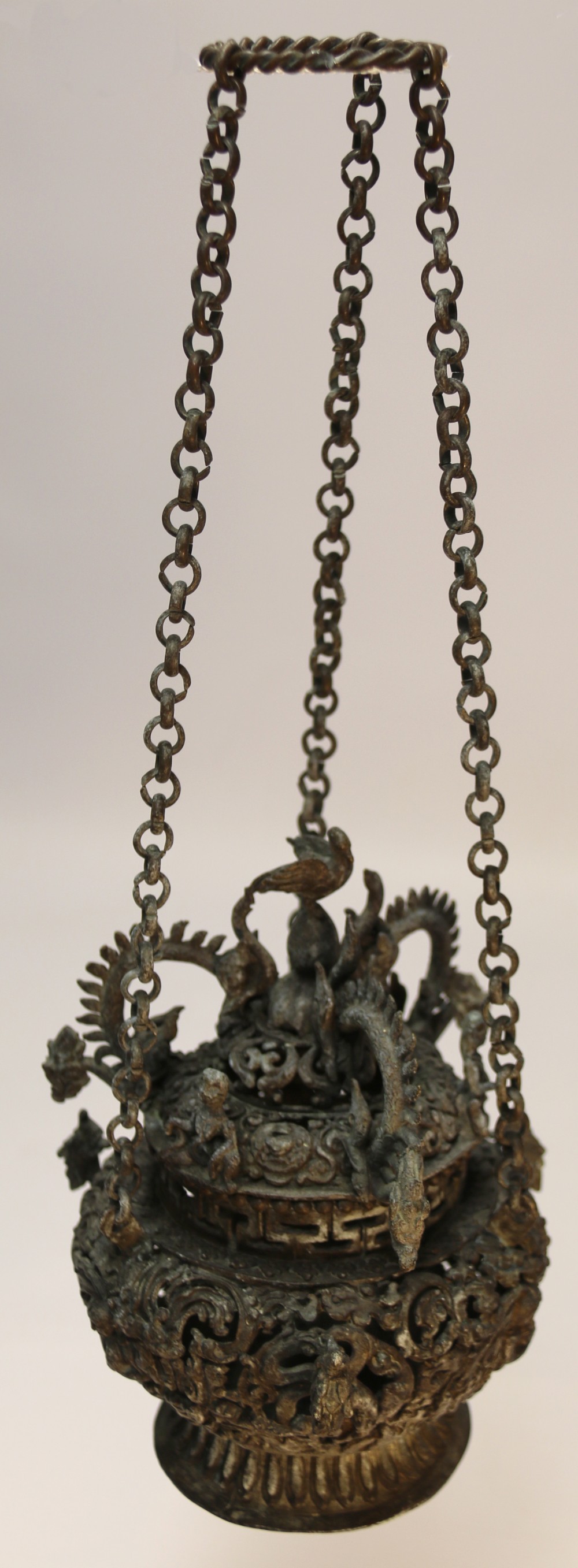 A dark patinated bronze hanging incense burner featuring dragon openwork motifs and a bird finial suspended by three link chains.