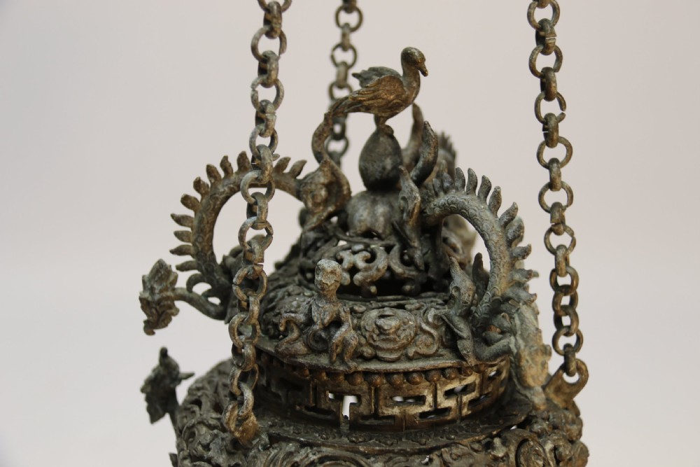 A dark patinated bronze hanging incense burner featuring dragon openwork motifs and a bird finial suspended by three link chains. View III