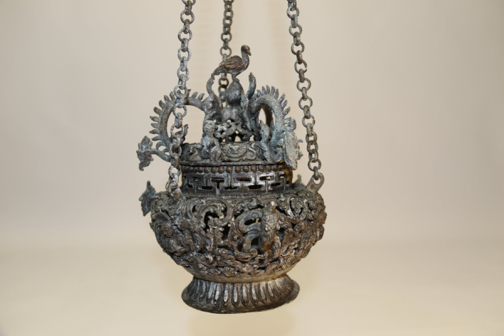 A dark patinated bronze hanging incense burner featuring dragon openwork motifs and a bird finial suspended by three link chains. View V